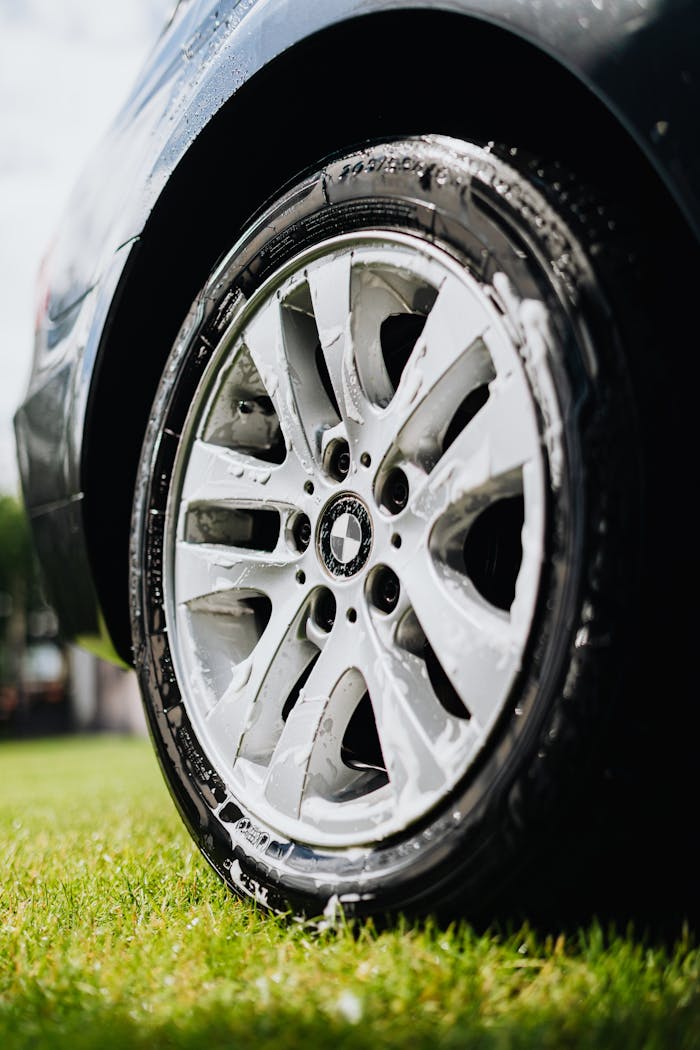 A detailed view of a car wheel being cleaned with soap on a sunny day.